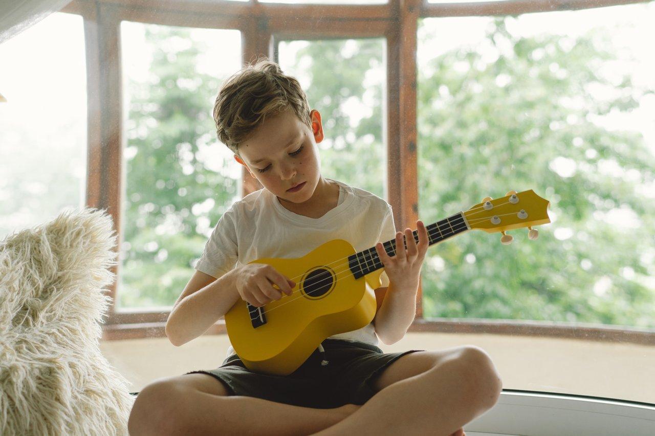 Enfant tenant deux ukulélés soprano et concert, illustrant la différence de taille pour débutants.