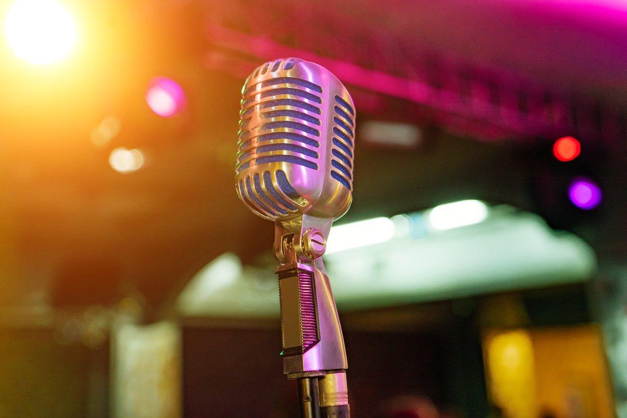 Microphone live concert Shure SM58 posé sur pied devant un chanteur en scène éclairée.