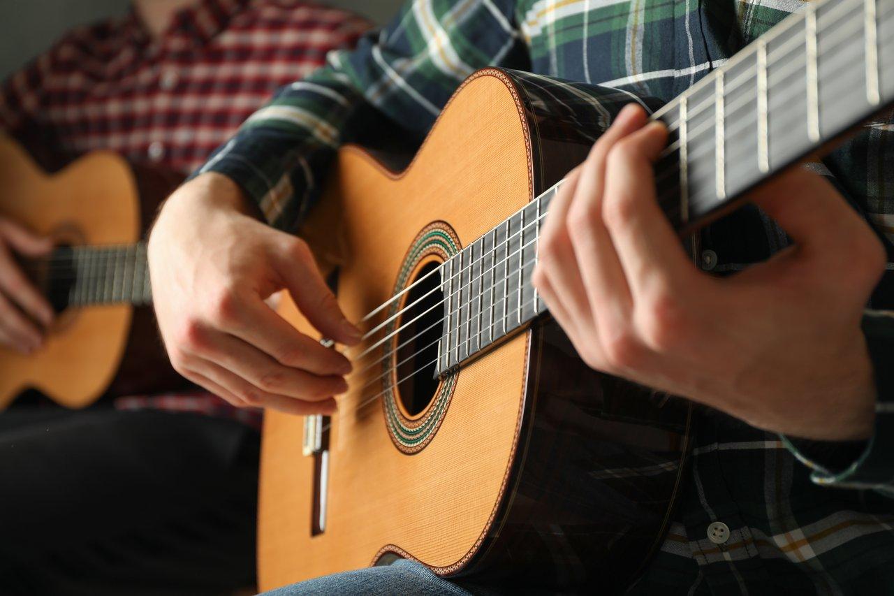 Un beginner acoustic guitar player pratique la lecture de grille d’accords pour accompagner une chanson pop.